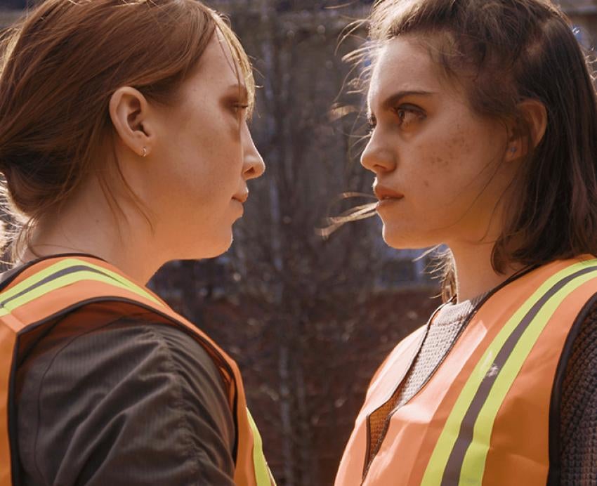 Two people wearing orange safety vests face each other