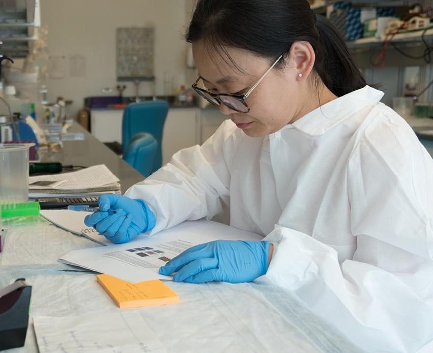 A researcher in gloves and a lab coat takes notes in the Aging Institute laboratory