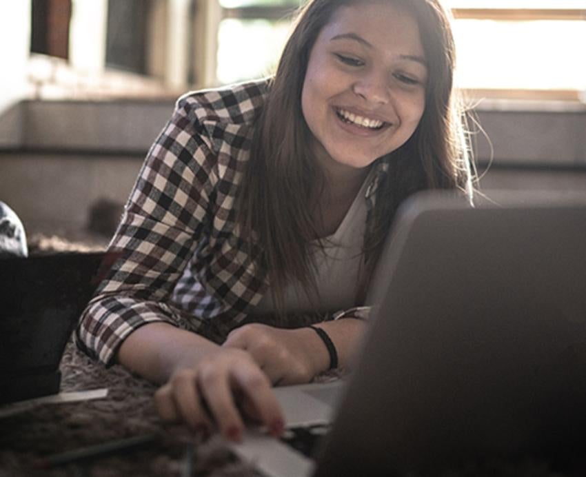A girl lays on the floor, smiling into her laptop
