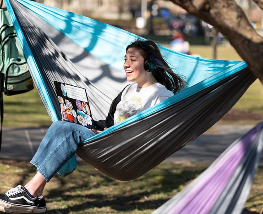 A student laughs while sitting in a hammock with a laptop