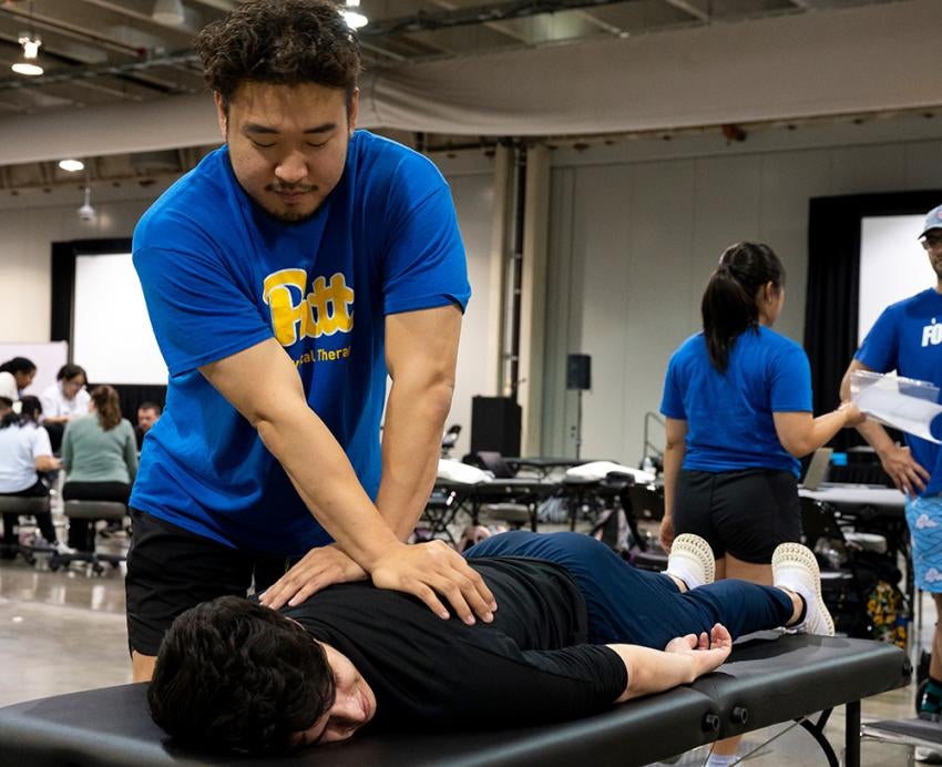 A physical therapy student holds his hands on a patient's back as they lay on table