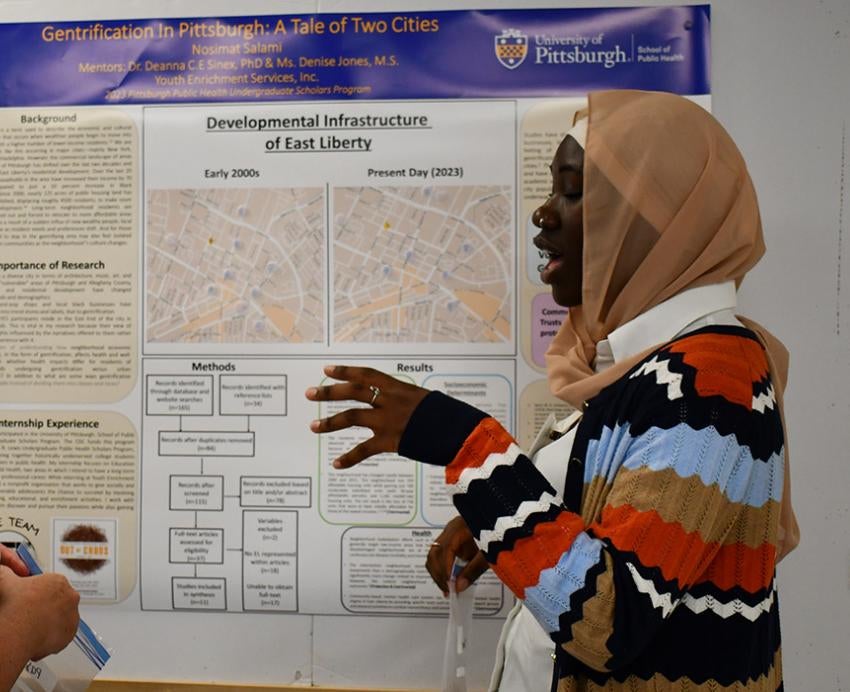 A student talks to a person about their research in front of a poster