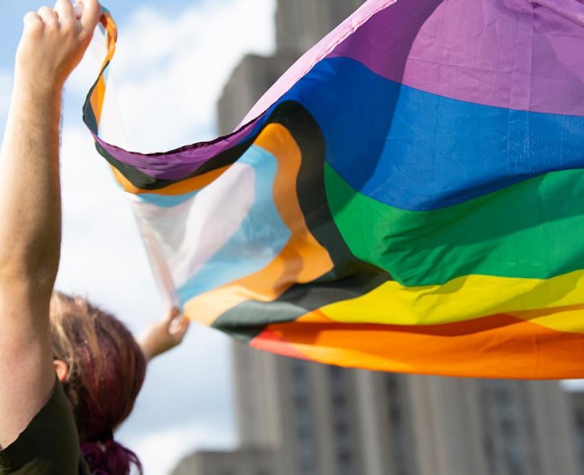 A person waves an LGBTQ+ pride flag in front of the Cathedral of Learning