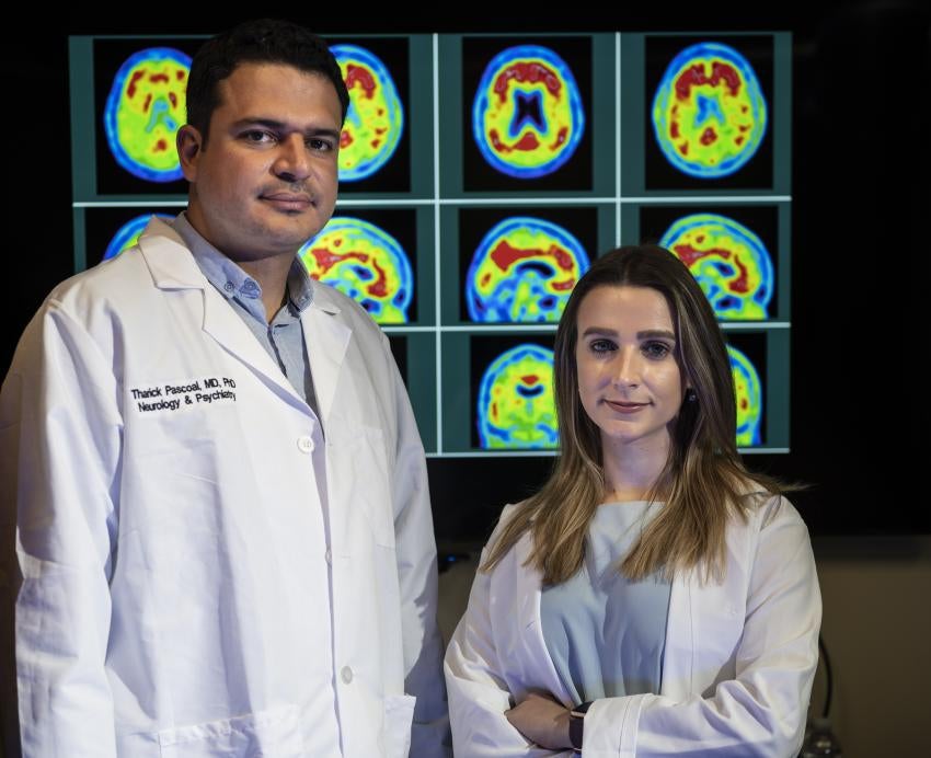 A man and a woman stand in front of pictures of brain scans.