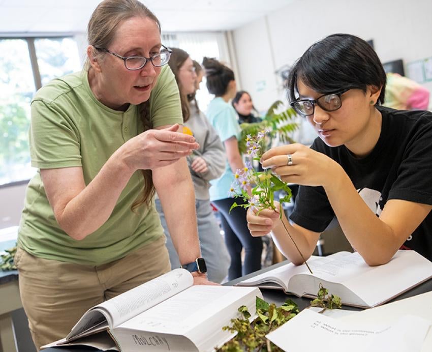 A teacher points at a plant a student is holding in a lab