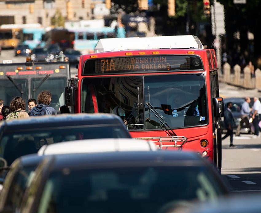 A red bus sits in traffic as people board