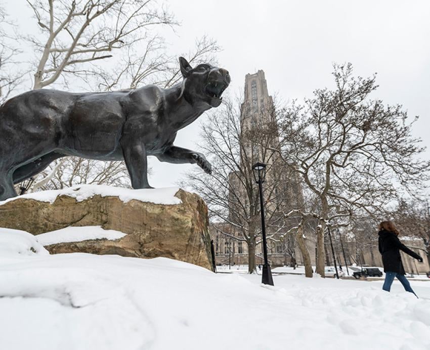 A panther statue on the snowy Pitt grounds. The Cathedral of Learning is in the background