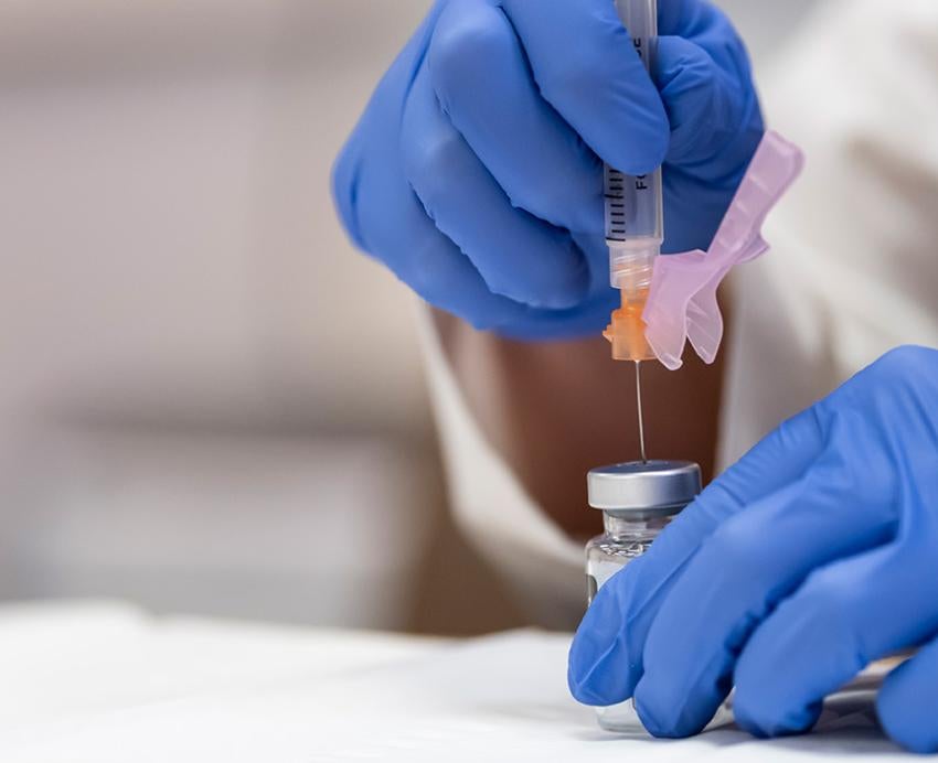 Gloved hands pull a vaccine into a syringe