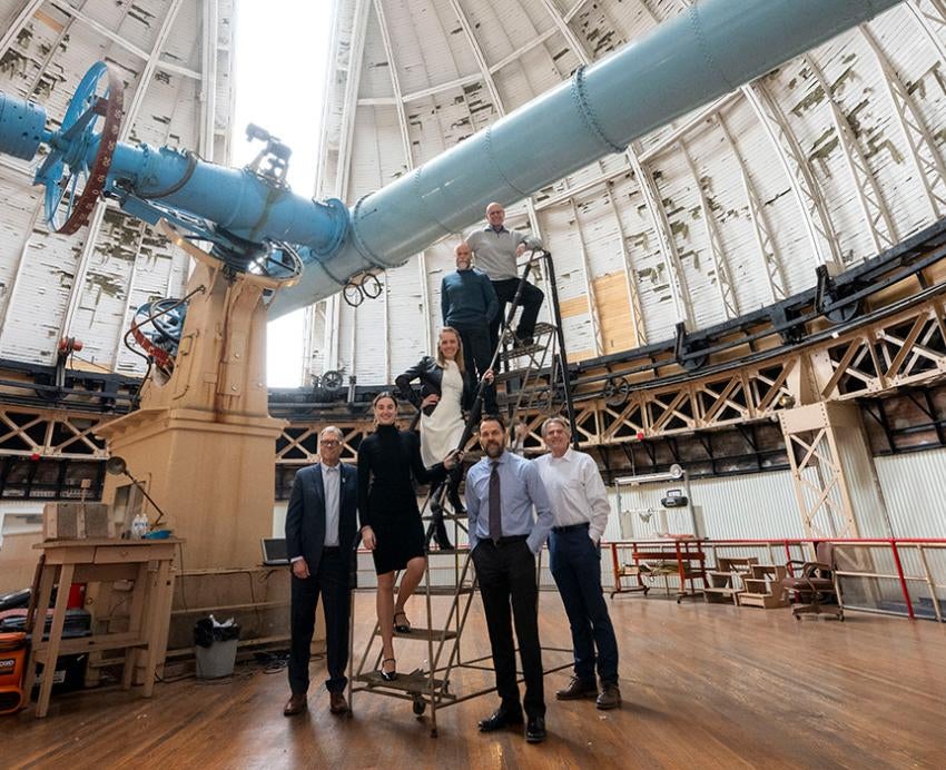 People stand on steps in a room housing a massive blue telescope