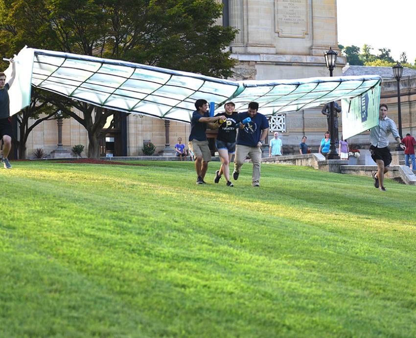 Students run with their glider on a lawn
