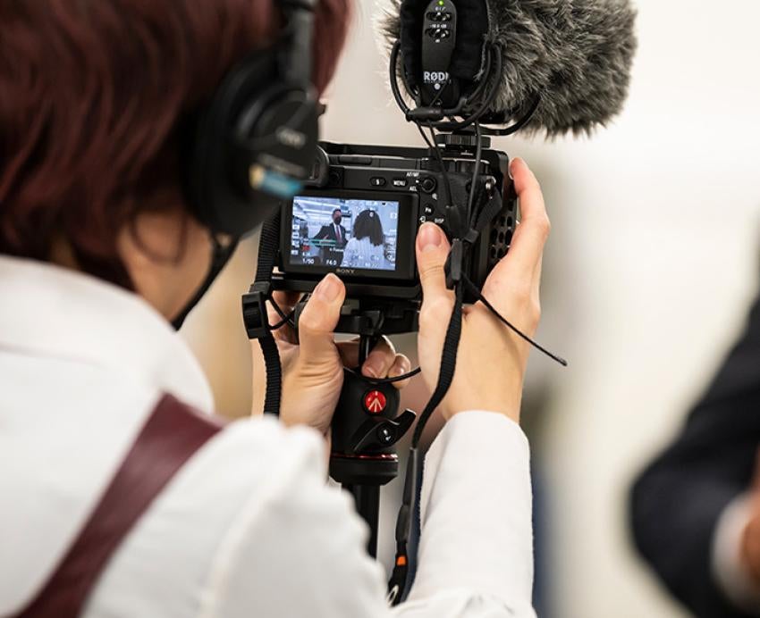 A person wearing headphones records others on a camera with a microphone attachment
