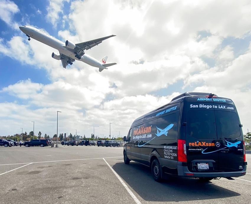 A reLAXsan van in an airport parking lot. A plane flies low overhead.