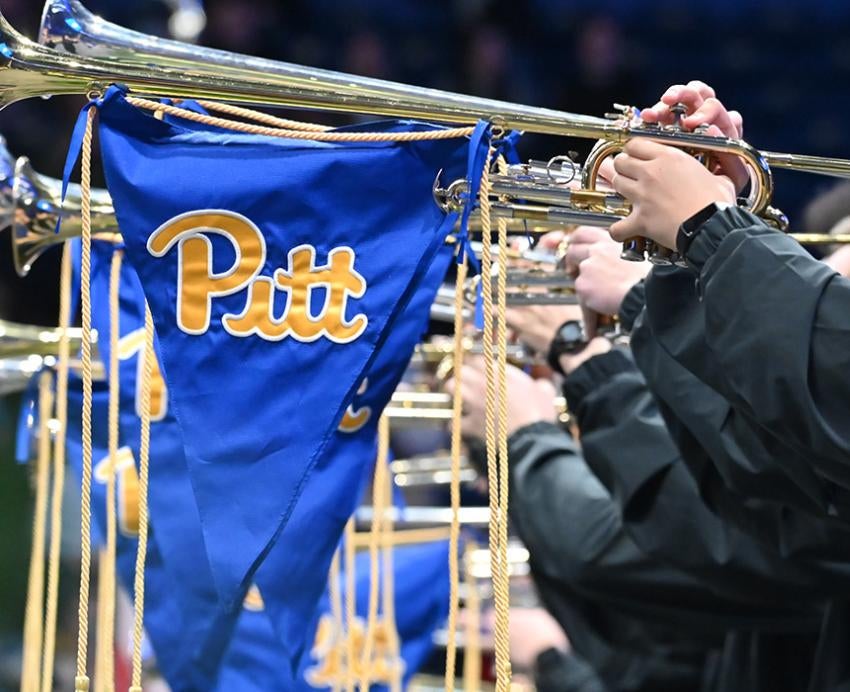 A line of people play horns with Pitt flags