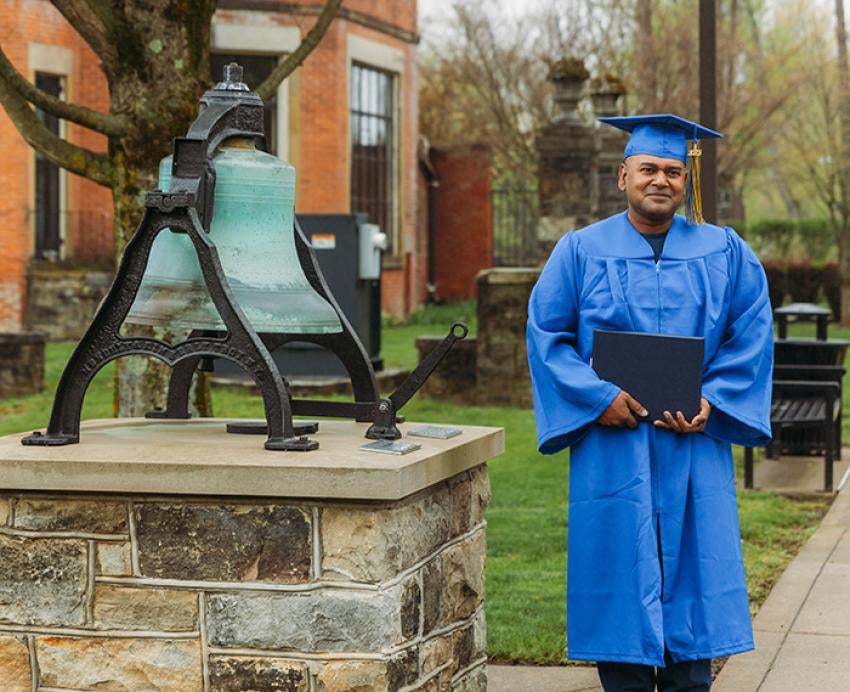 A graduate stands next to a large bell