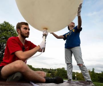 One student fills a large weather balloon with air while another holds it above her head