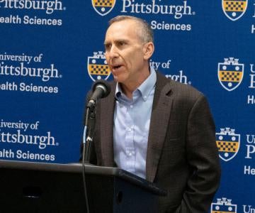 Michel Boninger speaks in front of a Pitt Health Sciences logo 