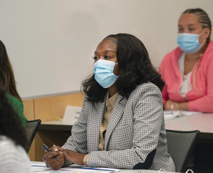 a woman taking notes in a checkered gray blazer wearing a blue mask