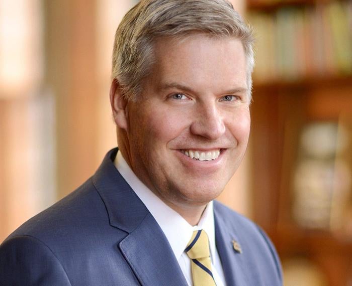 Patrick Gallagher smiling with navy blue suit and yellow tie