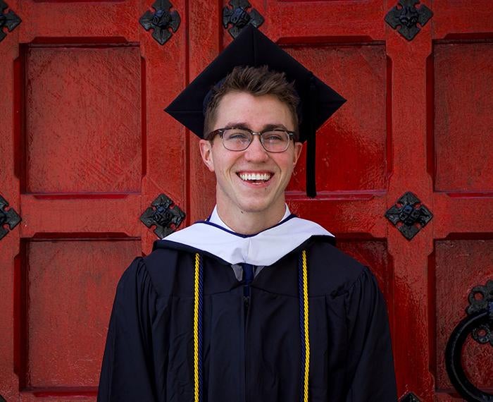 Chandler Mitchell wearing cap and gown in front of large red door