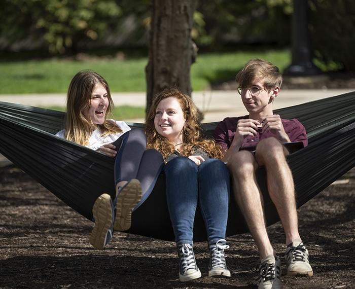 Three students sitting on hammock together