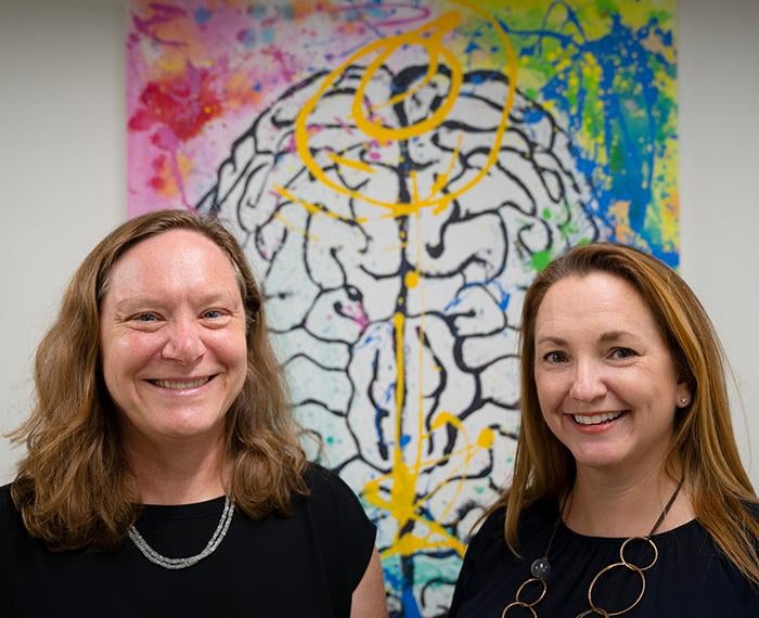 the two new leaders in front of a colorful illustration of a brain