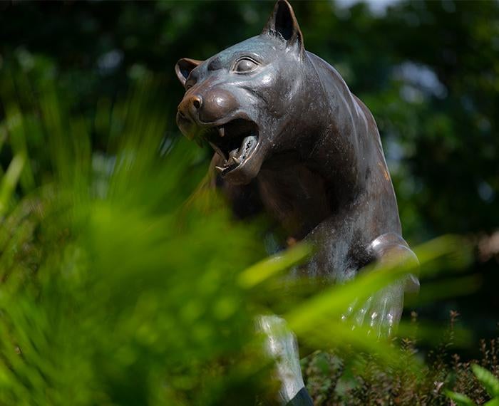 a panther statue peeking out from some green plants