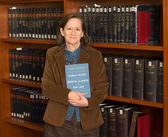 Linda Tashbook holds her book in front of shelves