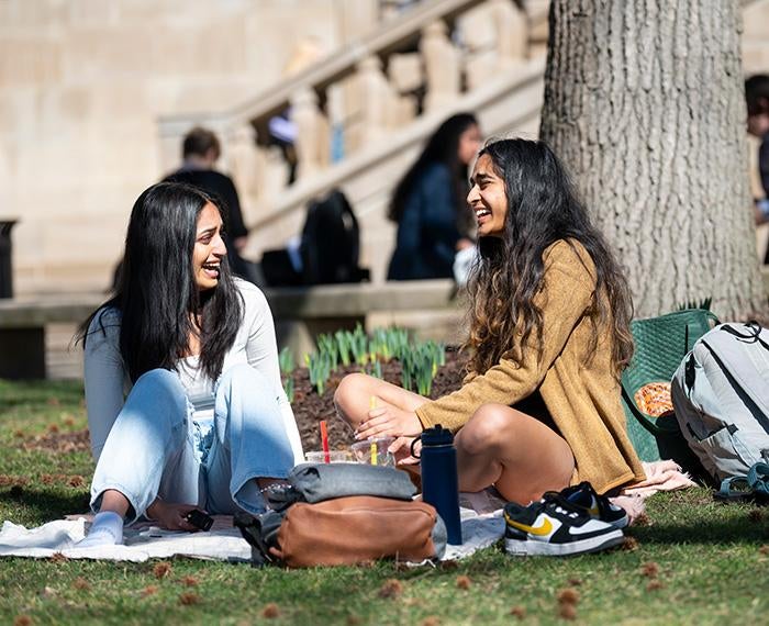 Two students sitting in the grass laugh