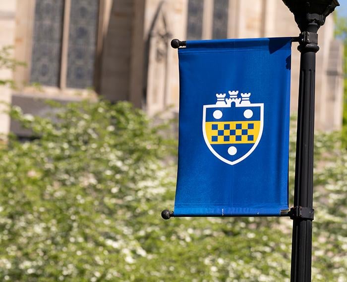 A blue flag with a Pitt shield in front of the Cathedral of Learning