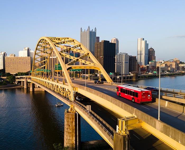 A bus travels over a yellow bridge into downtown Pittsburgh