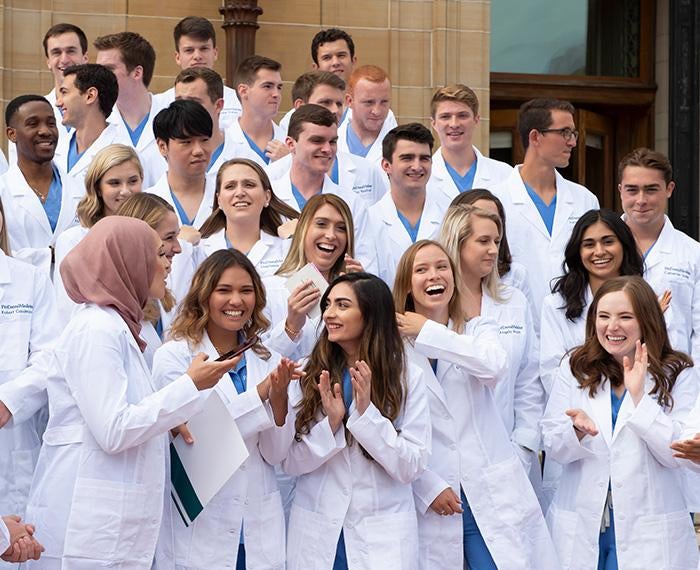 A group of dental students pose on steps in their white coats