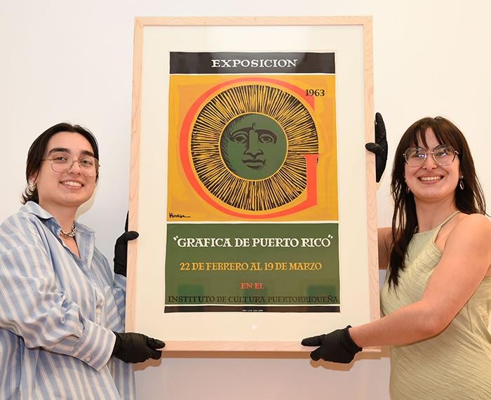 Two students lift a poster for the Grafica de Puerto Rico exhibit