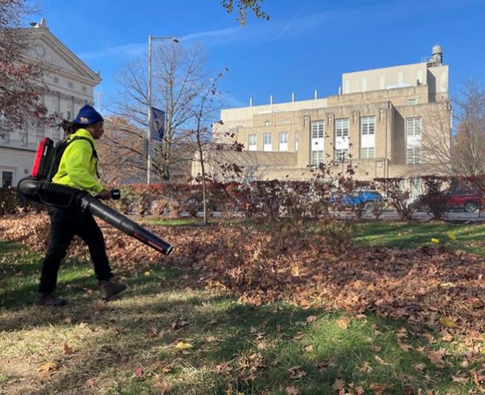 A person moves leaves into a pile using a backpack leaf blower.