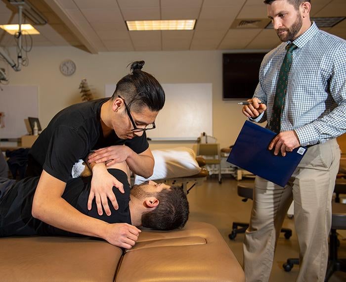 An instructor with a clipboard watches a physical therapy examination