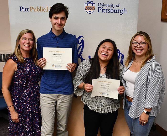 Two high school students hold certificates beside their mentors