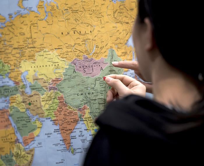 A person in black puts a mark on a map of the world