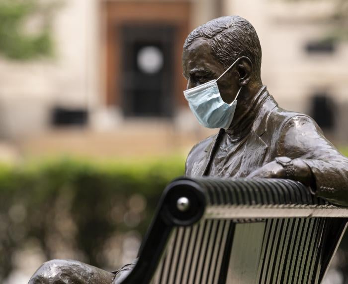 A statue sitting on a bench with a face mask