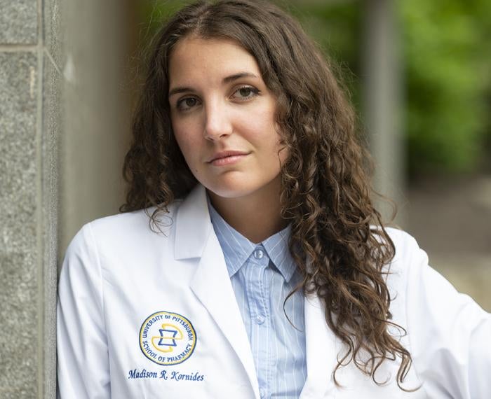 Madison Kornides, in a white lab coat leaning against a stone wall