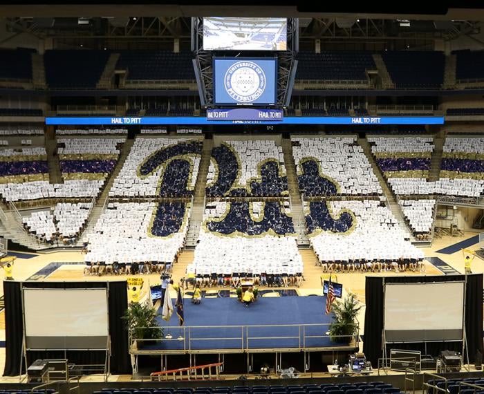 Pitt script logo created by class of 2016 members holding signs in Petersen Events Center