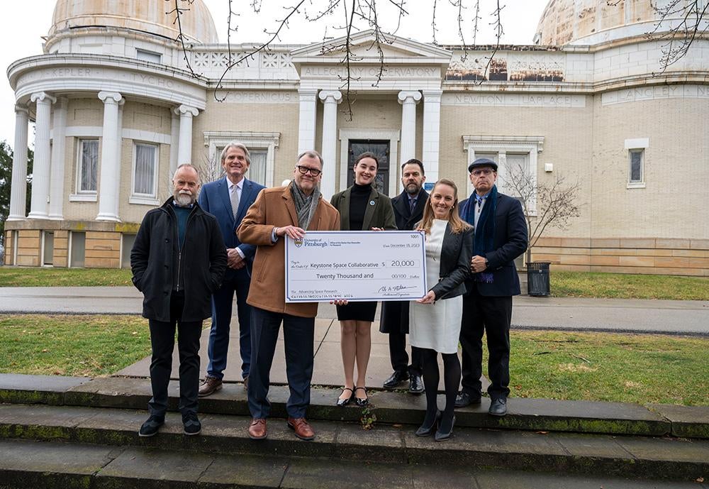 A group of people pose with a check in front of Allegheny Observatory