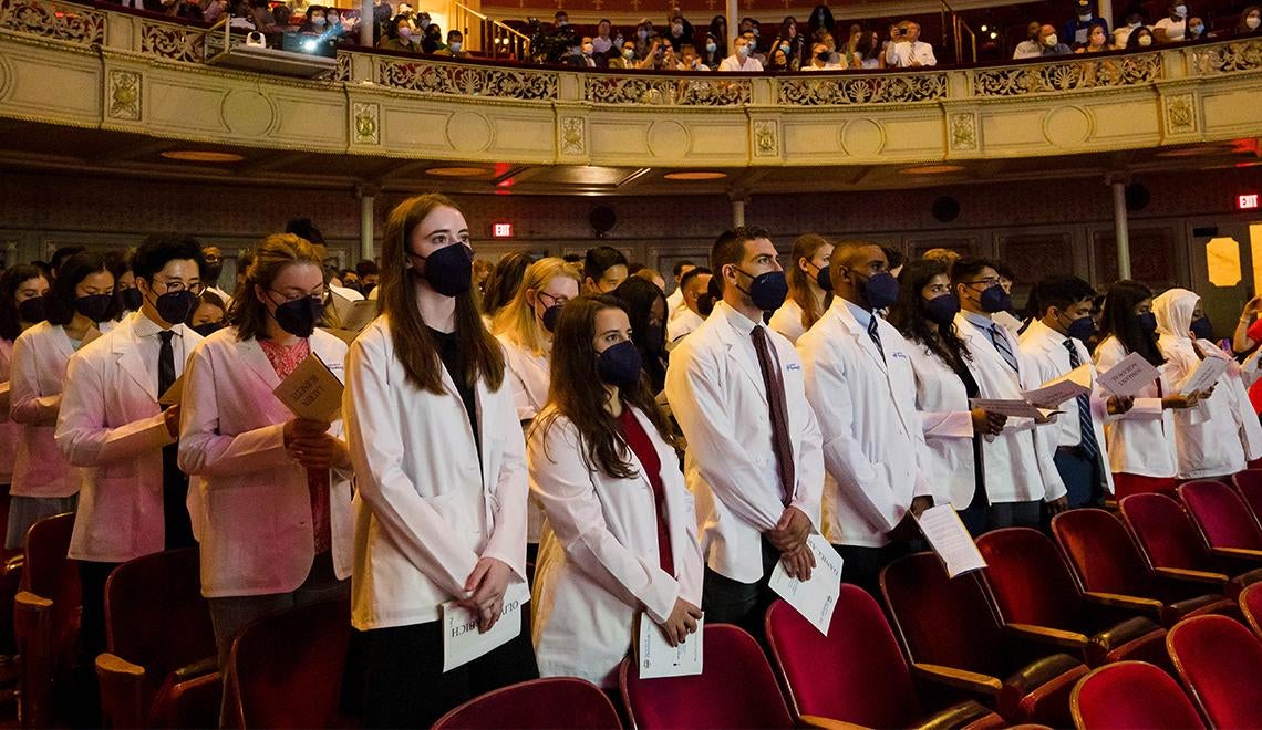 a group of people wearing white coats and masks in an auditorium