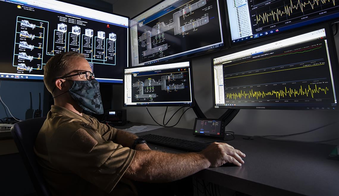 Man with mask using computer with five monitors