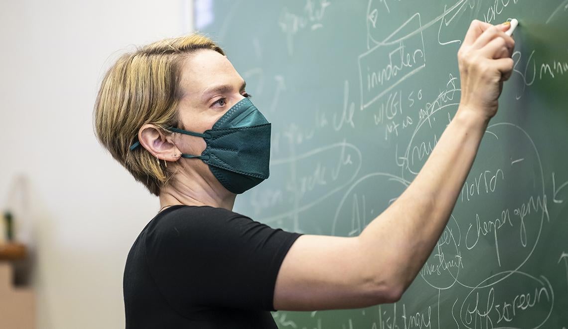 Dana Och writing on chalkboard while wearing face mask