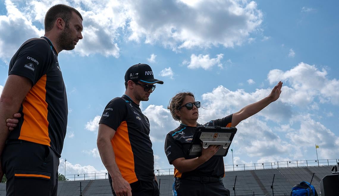 Two racers look at Gundlach's tablet as she points at the track
